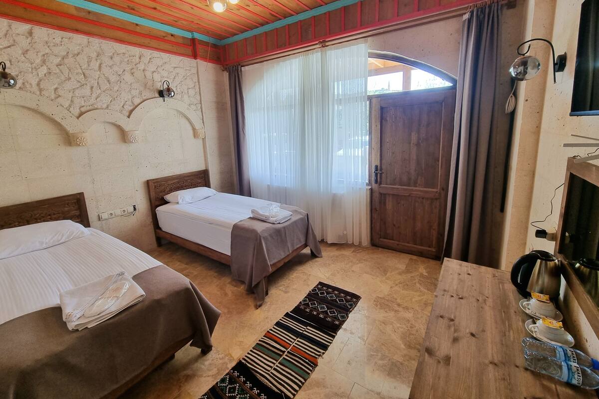 A room with two beds, a wooden ceiling, a patterned rug, and a wooden table with a kettle and cups.
