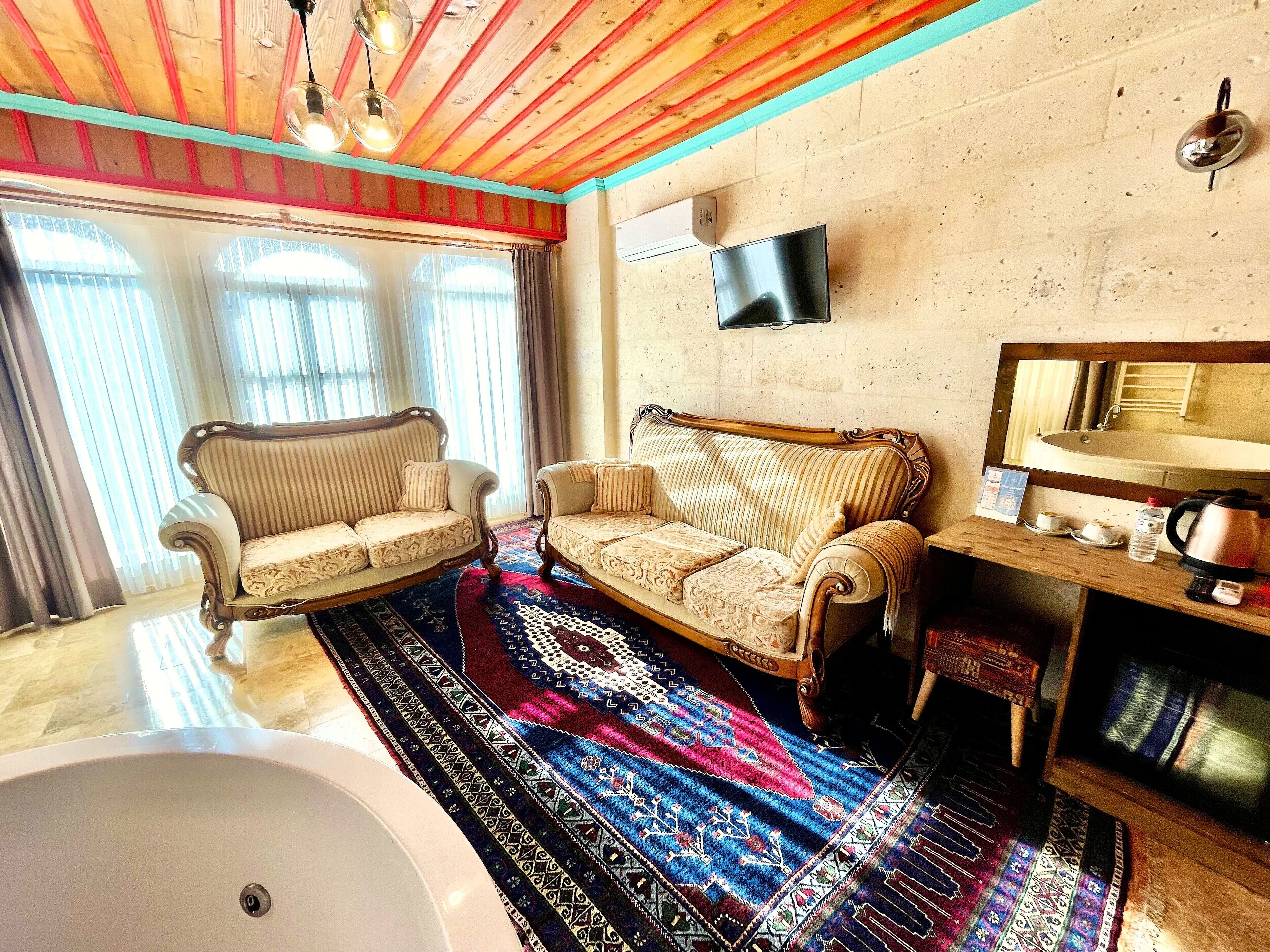 A room with a large bathtub, two sofas, a patterned rug, and a mounted television.