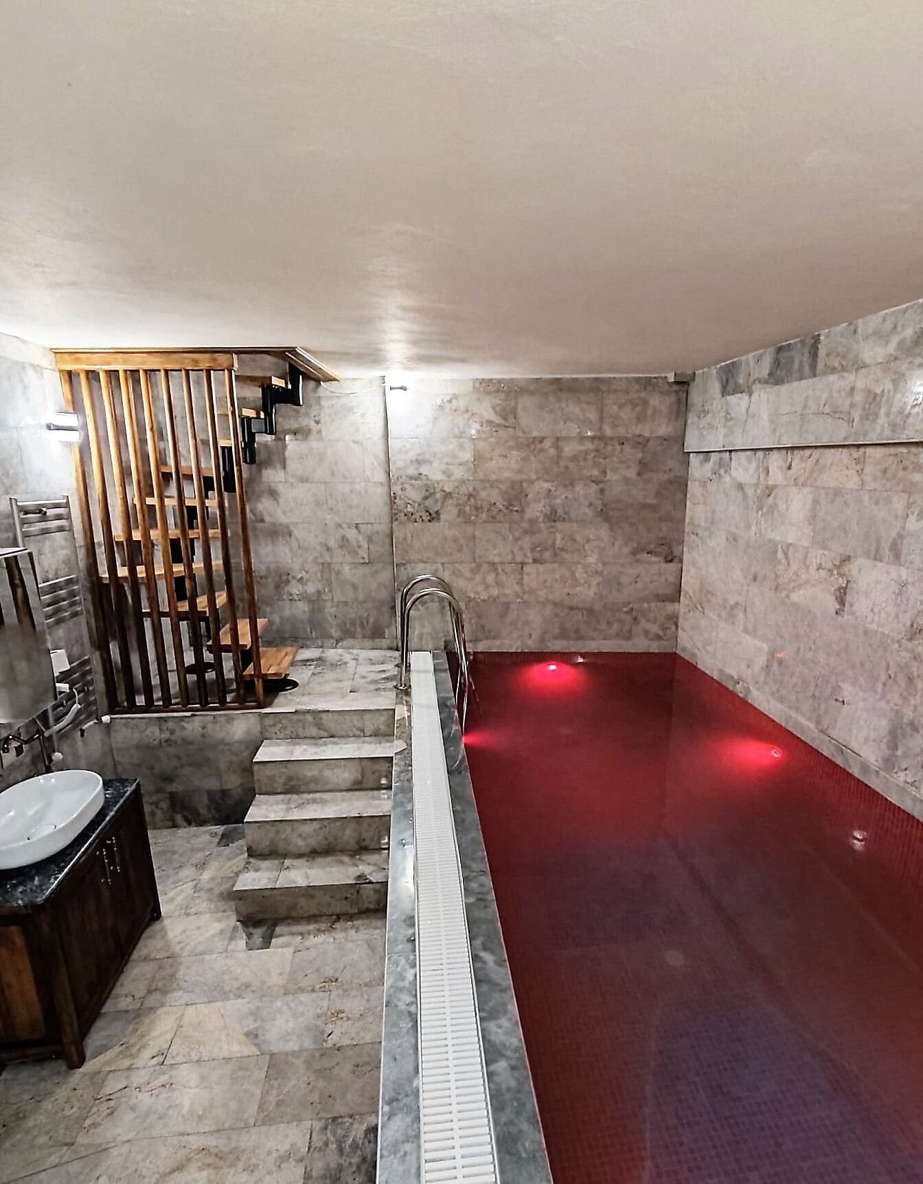 Un baño moderno con piso de mármol, suelo calefaccionado rojo, cabina de ducha con paneles de madera y un lavamanos blanco con encimera oscura.