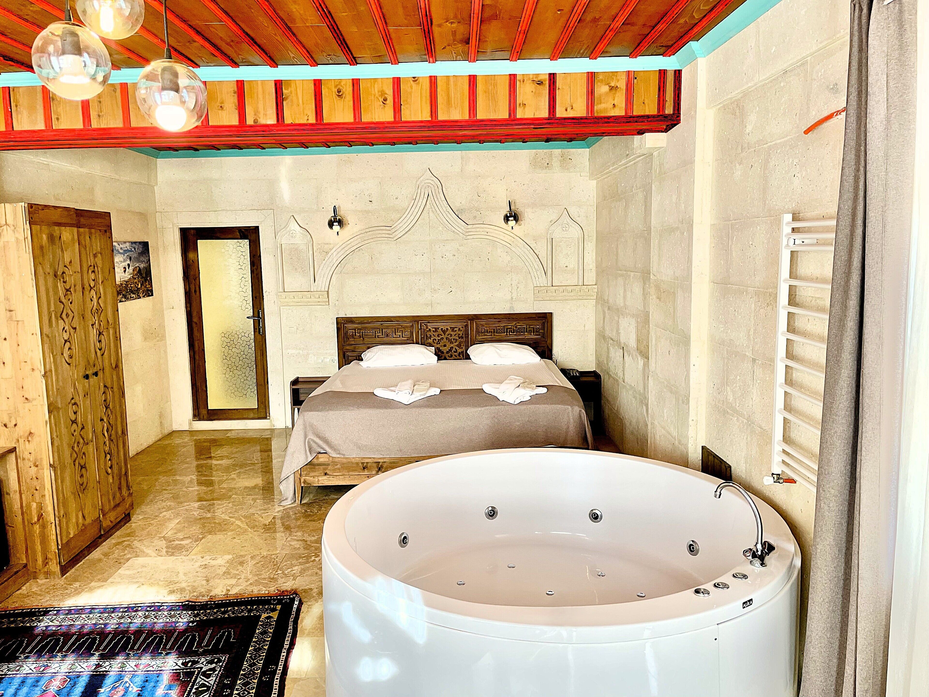 Une chambre d’hôtel avec une grande baignoire, une porte en bois, un lit avec une tête de lit et un luminaire fixé au mur.