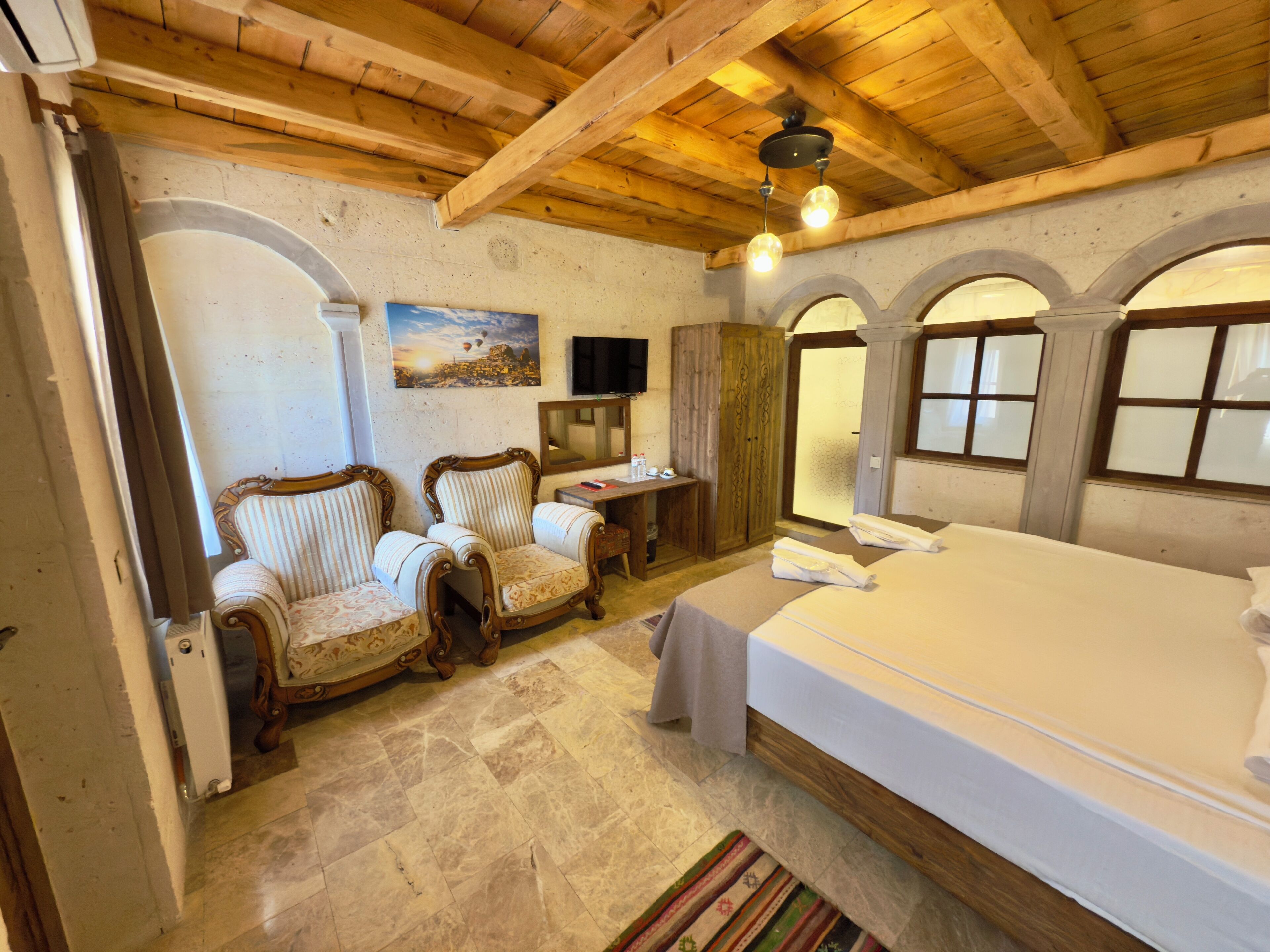 A bedroom with a large bed, two upholstered chairs, a small table, a mirror, and a painting on the wall.