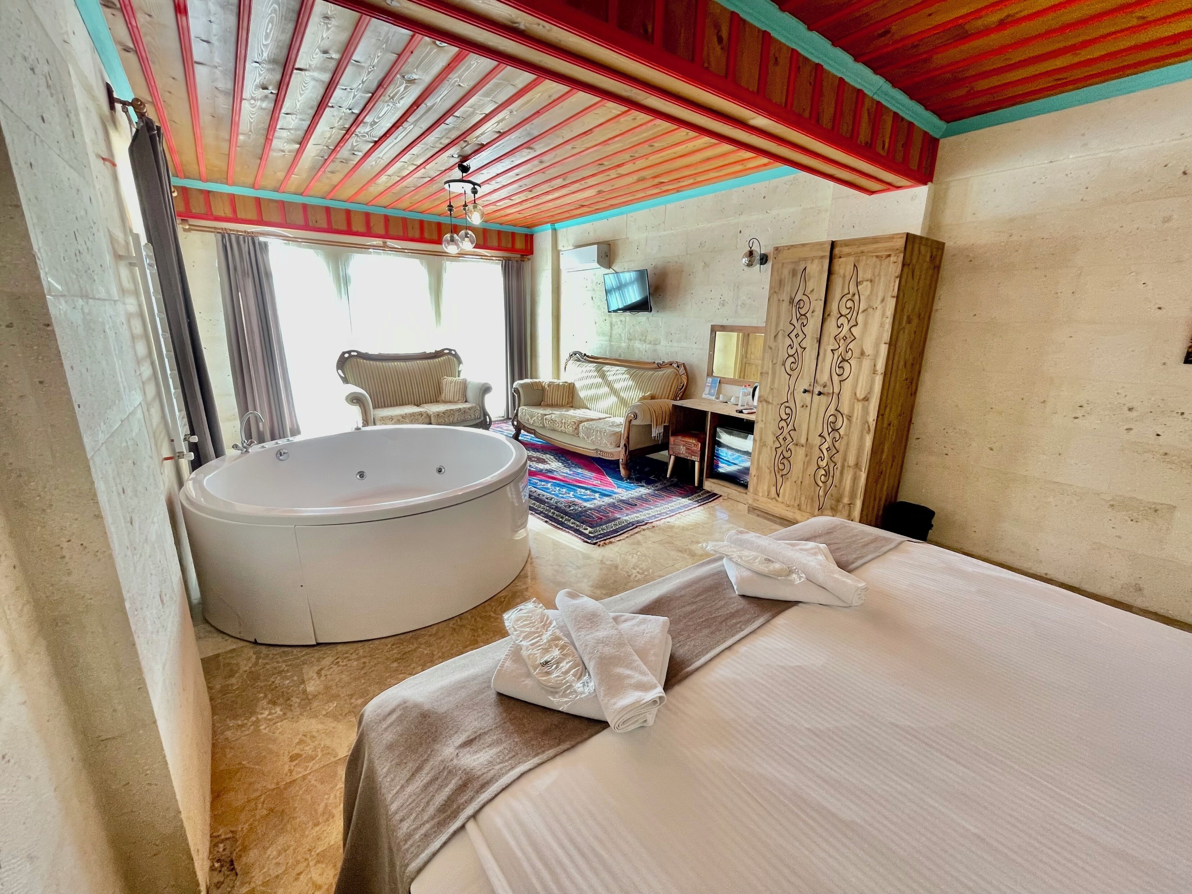 Une chambre d’hôtel avec une grande baignoire, un lit avec des serviettes, un canapé et une télévision.