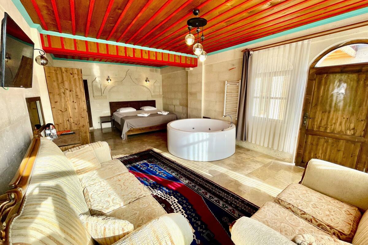 A spacious room with a large bed, a round bathtub, and a seating area with patterned cushions.