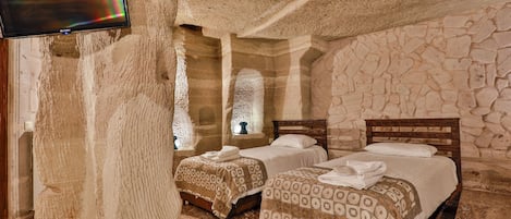 A stone-walled bedroom with two beds, a flat-screen TV, and a stone ceiling.