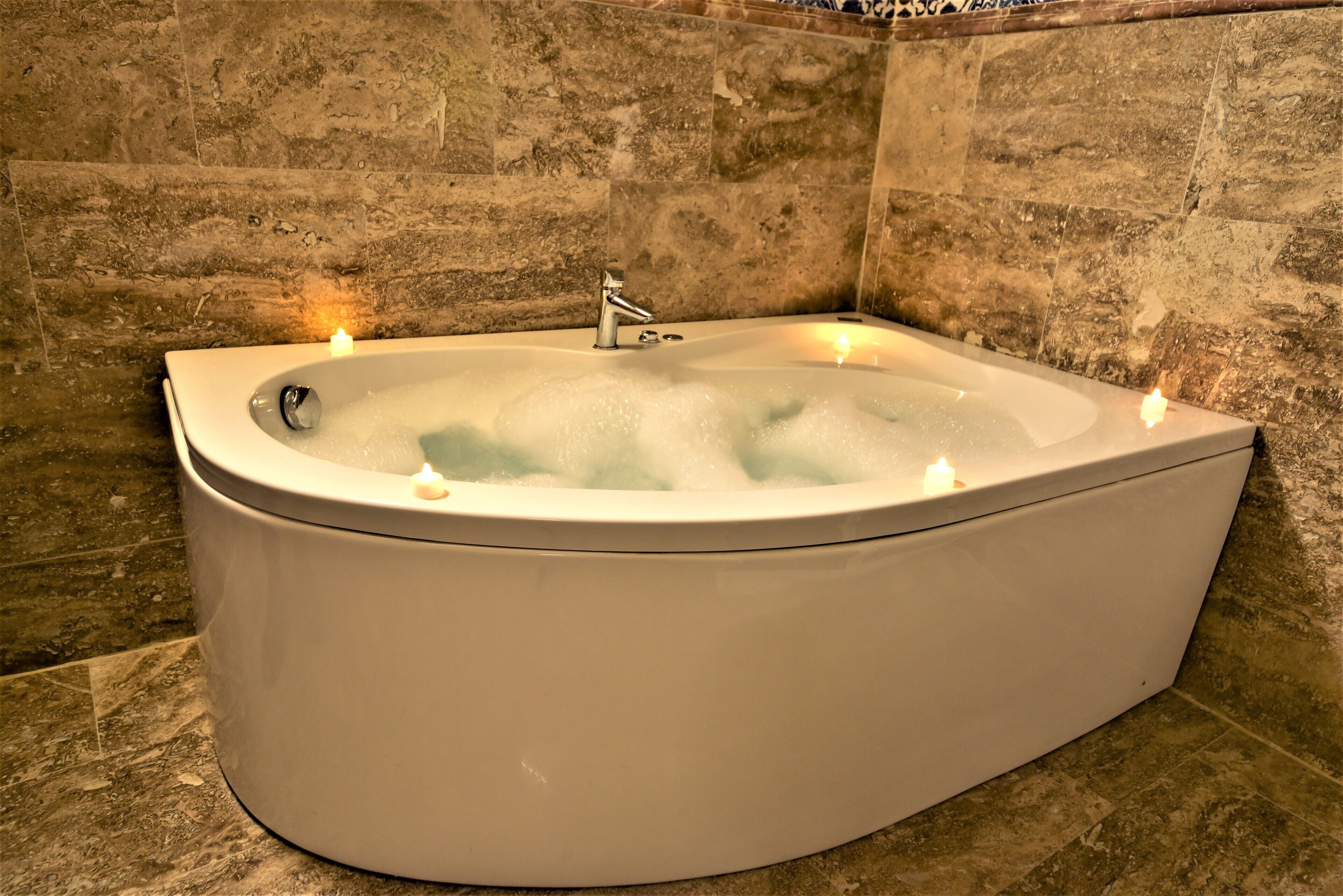 A large, freestanding bathtub with a modern faucet, surrounded by stone tiles.