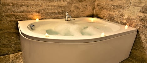 A large, freestanding bathtub with a modern faucet, surrounded by stone tiles.