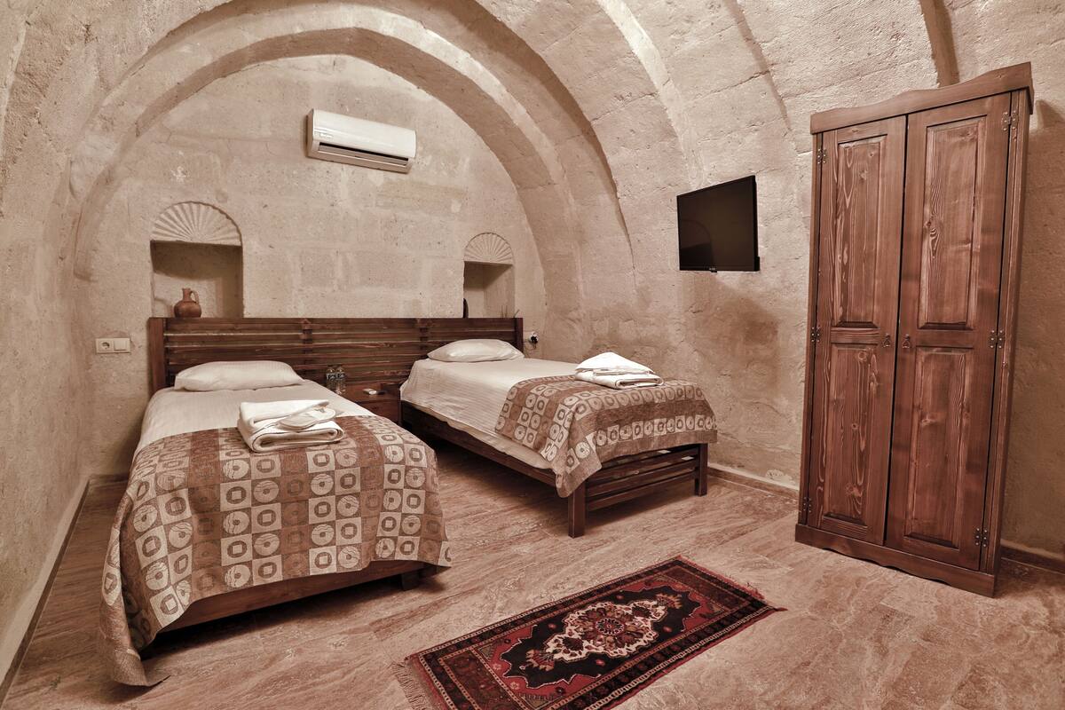A room with two beds, a wooden wardrobe, and a patterned rug.