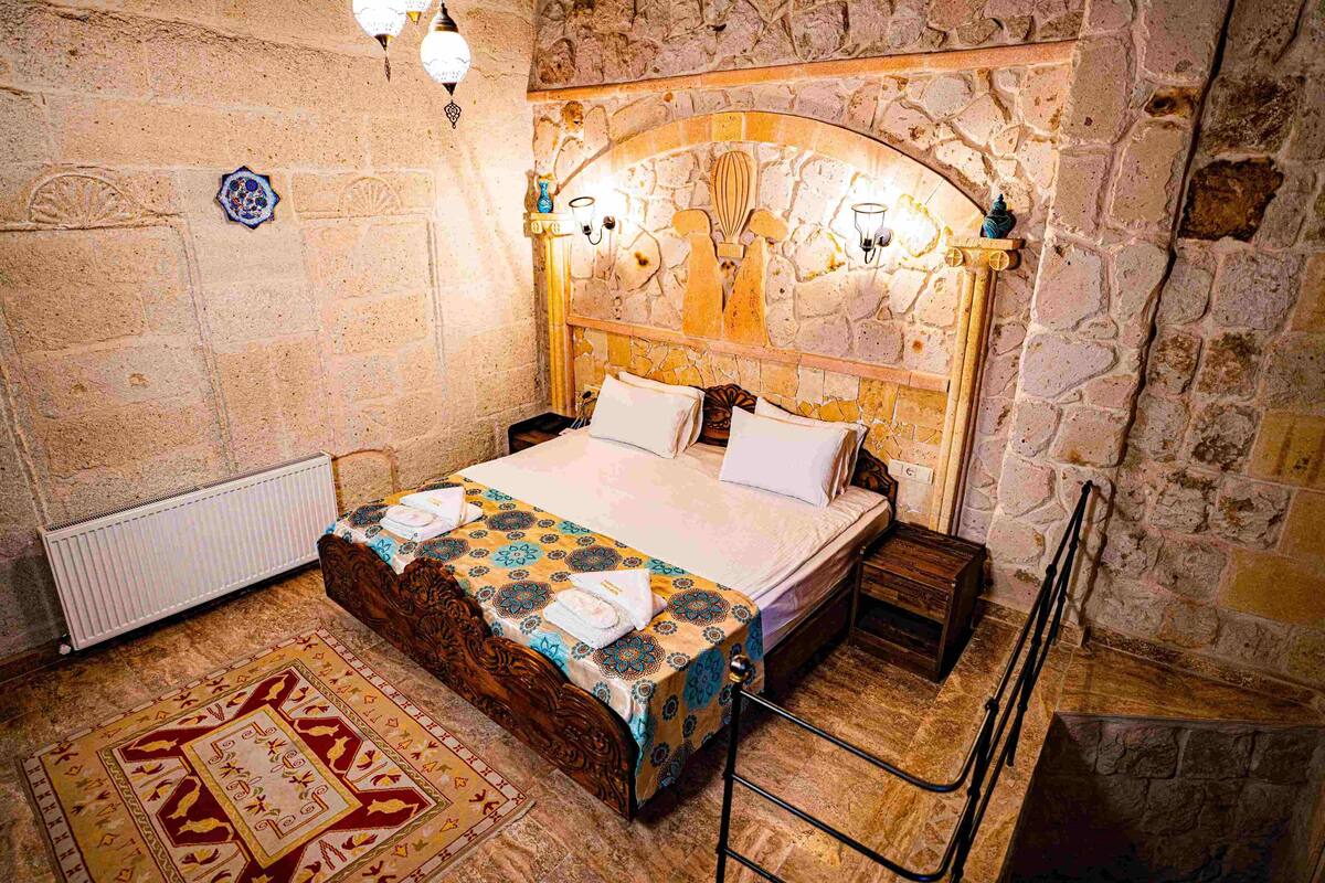 A traditional room with a stone wall, a wooden bed with a patterned bedspread, a radiator, and a decorative rug.
