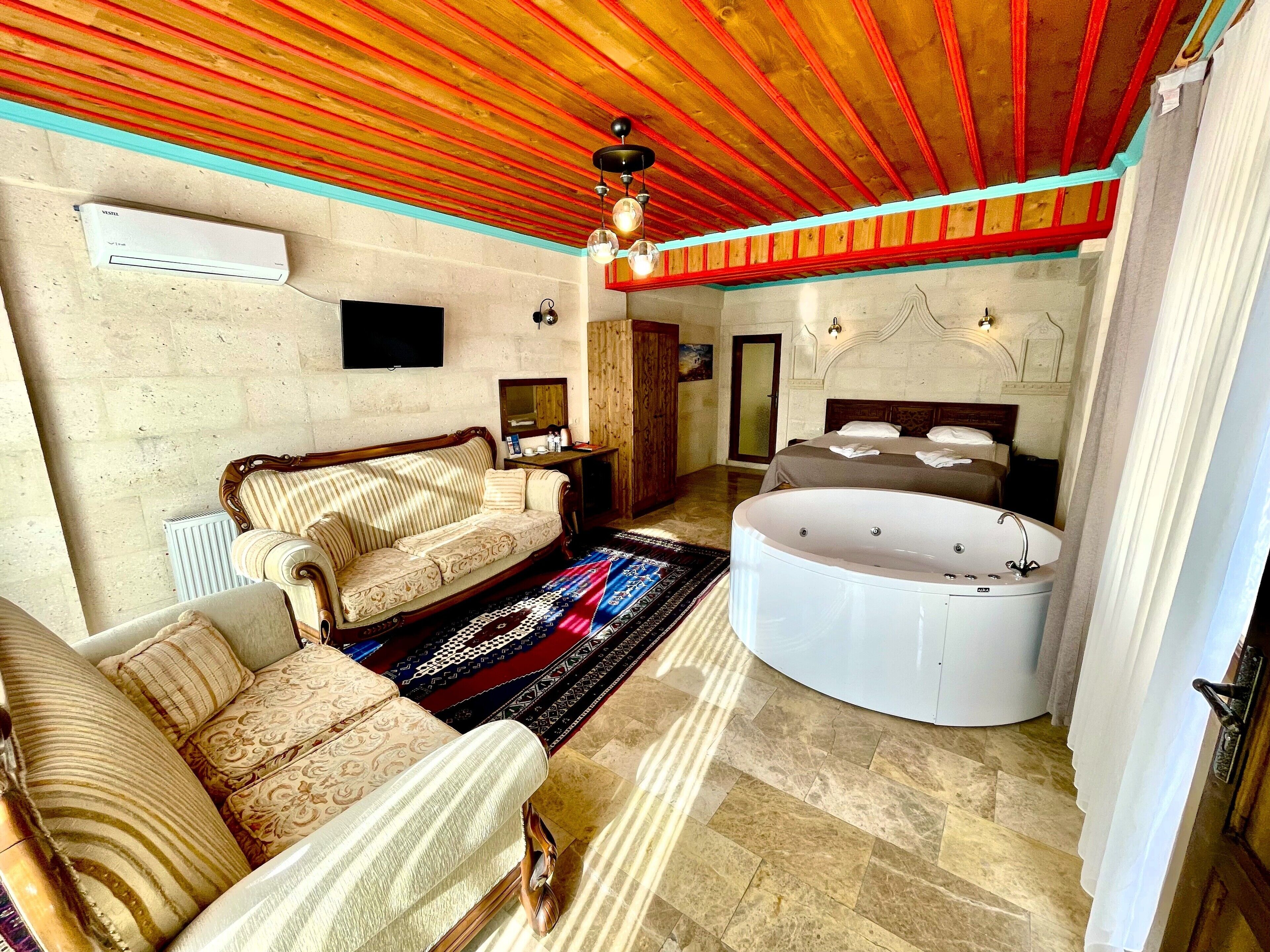 A spacious room with a wooden ceiling, a large sofa, a round bathtub, and a television on the wall.