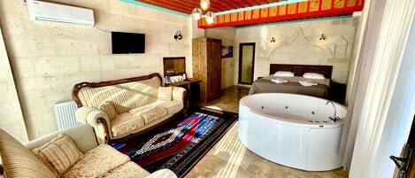 A spacious room with a wooden ceiling, a large sofa, a round bathtub, and a television on the wall.