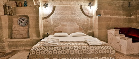 A stone-walled room with a bed, a stone fireplace, and a small shelf with decorative items.