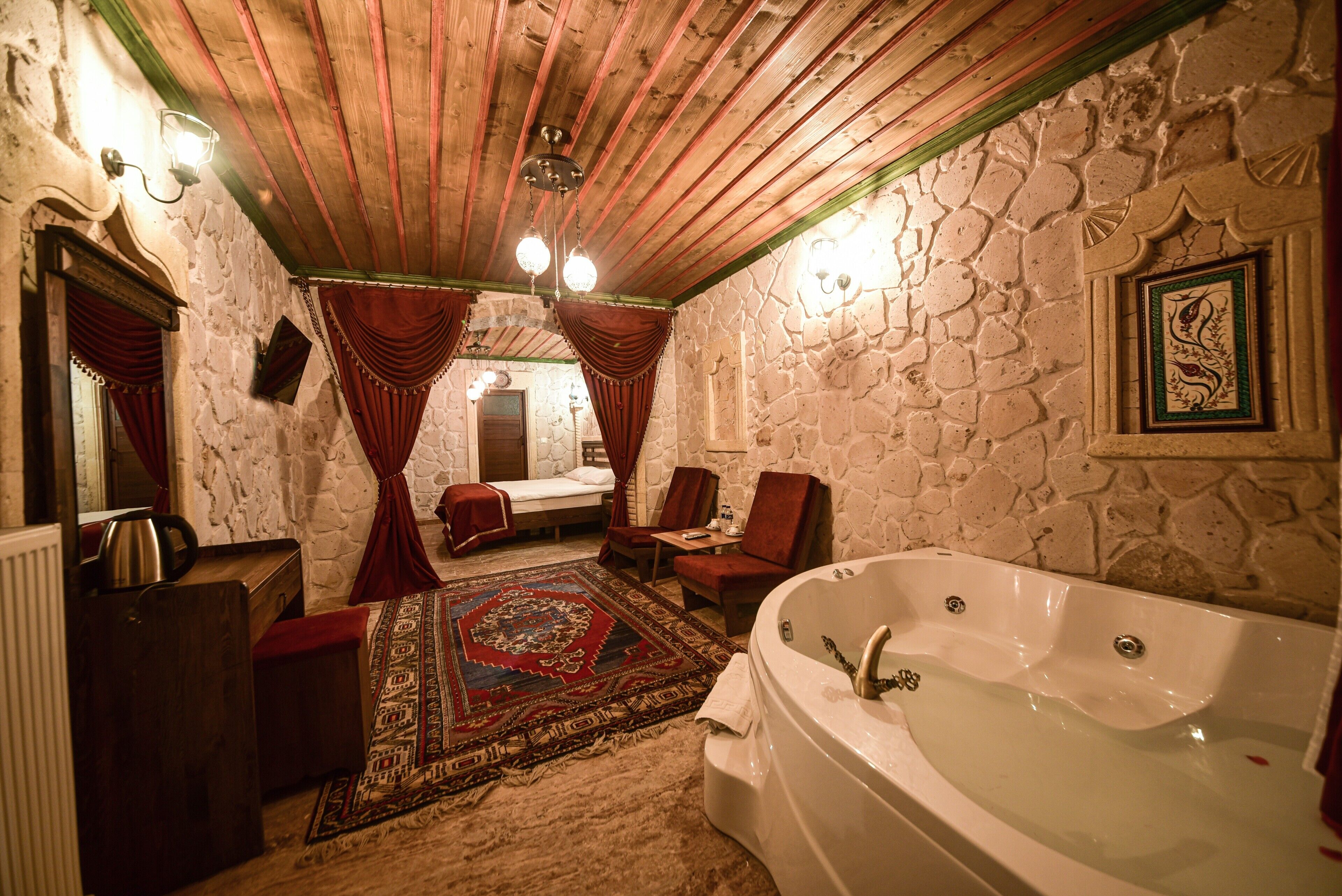 A room with a stone wall, a large bathtub, a wooden ceiling, and a red carpet.