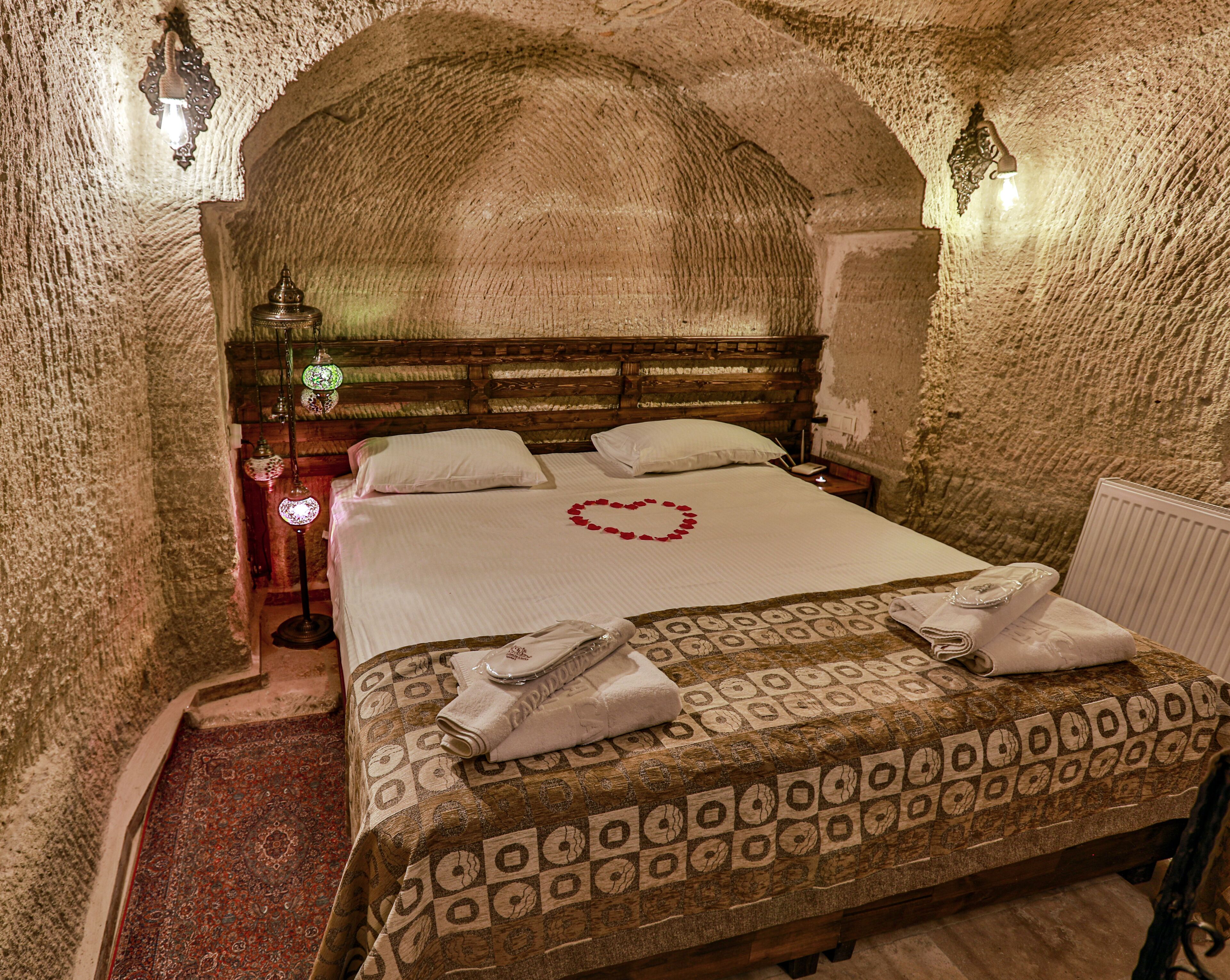 A room with a stone wall, a wooden bed with a heart-shaped decoration, and a patterned bedspread.