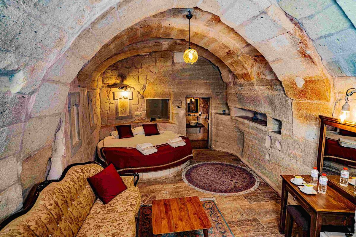 A cozy, stone-walled room with a bed, sofa, and a small table, featuring a rustic ambiance.