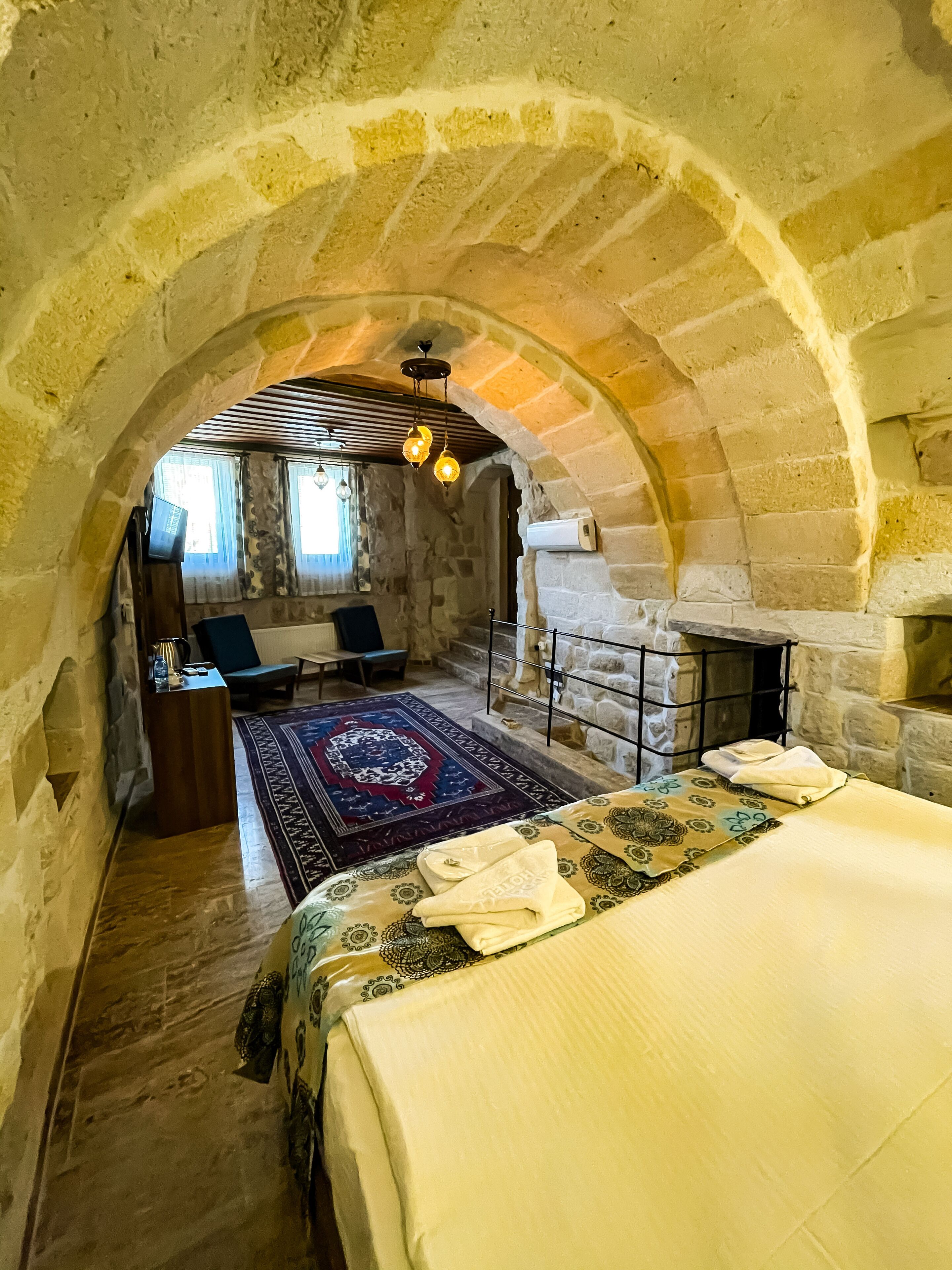 A stone-walled room with a bed, a fireplace, and a view through an arched doorway.