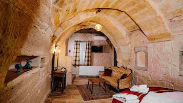 A stone-walled room with a sofa, a small table, a radiator, and a television.