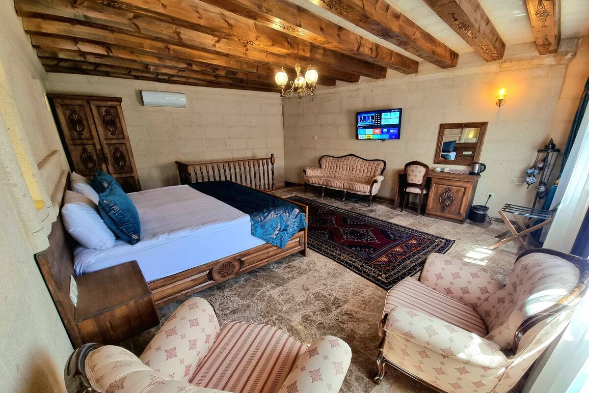 A room with a bed, two armchairs, a sofa, a TV, and a wooden ceiling.