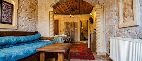 A stone-walled room with a wooden bench, a table, and a red carpet leading to a door.