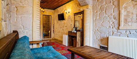 Una habitación con paredes de piedra, un banco de madera, una mesa pequeña y una alfombra colorida.