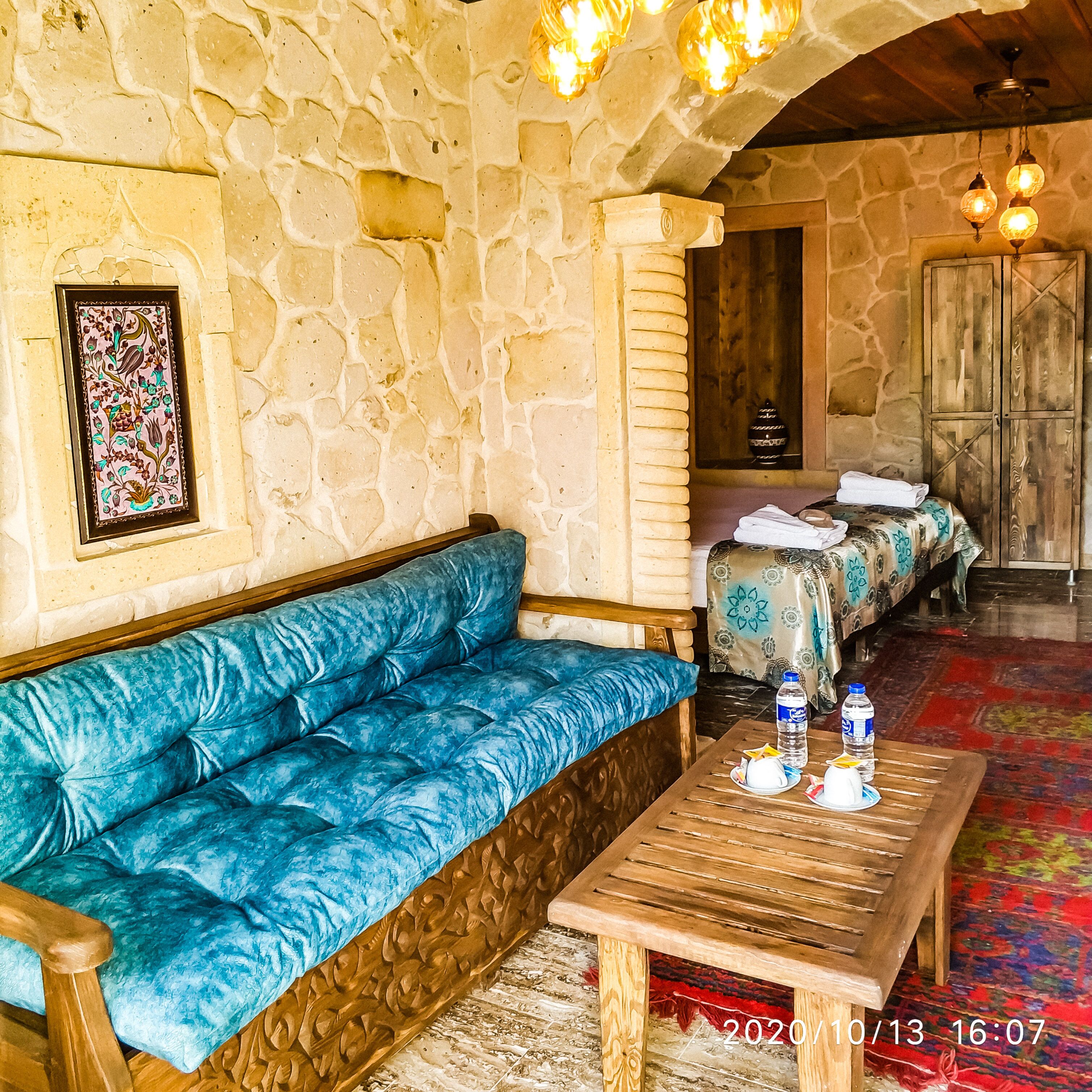 A stone-walled room with a blue cushioned sofa, a wooden table with a bottle and a cup, and a patterned tablecloth.