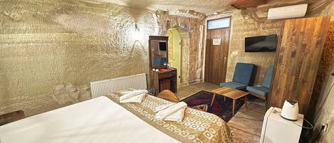 A room with a bed, a desk, a chair, a TV, and a small table.