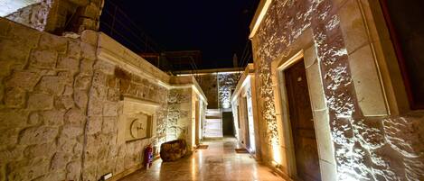 A stone-walled corridor with a fire extinguisher, a red vase, and a staircase leading to a lit upper level.