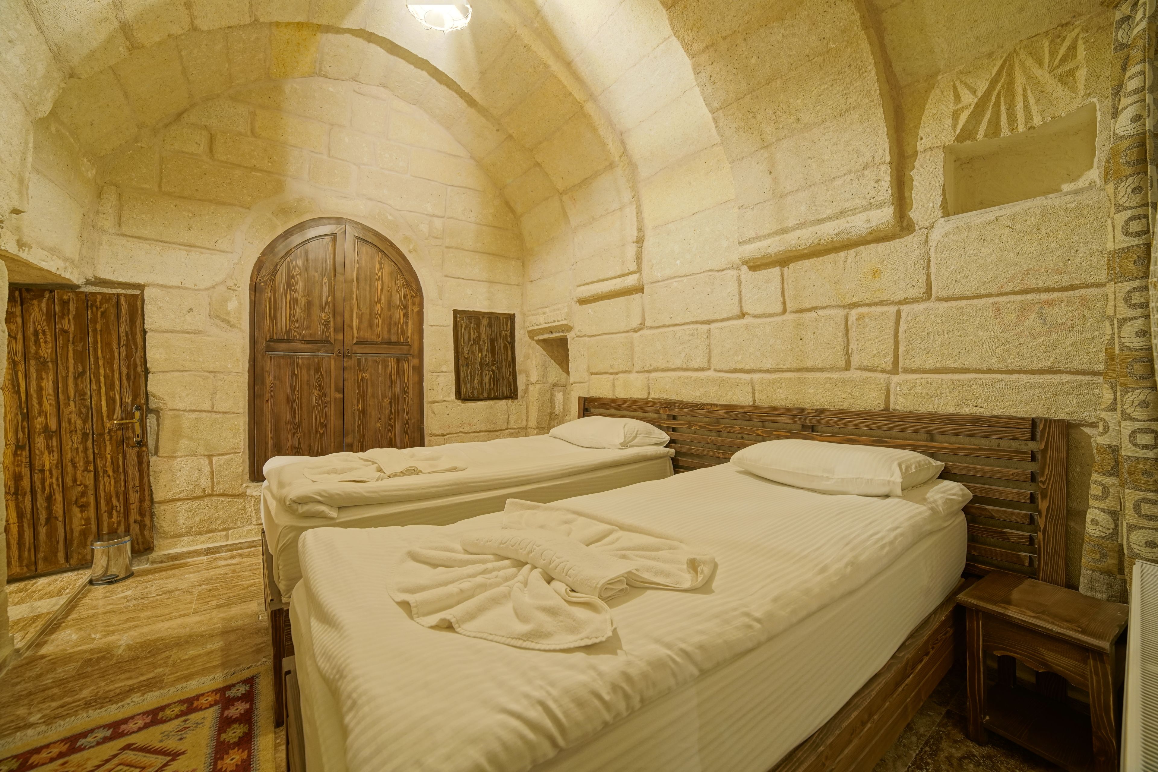 Una habitación con dos camas, paredes de piedra, puertas de madera y suelo de baldosas.