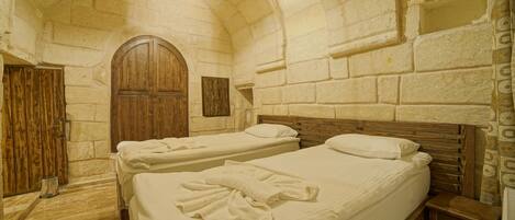 Una habitación con dos camas, paredes de piedra, puertas de madera y suelo de baldosas.