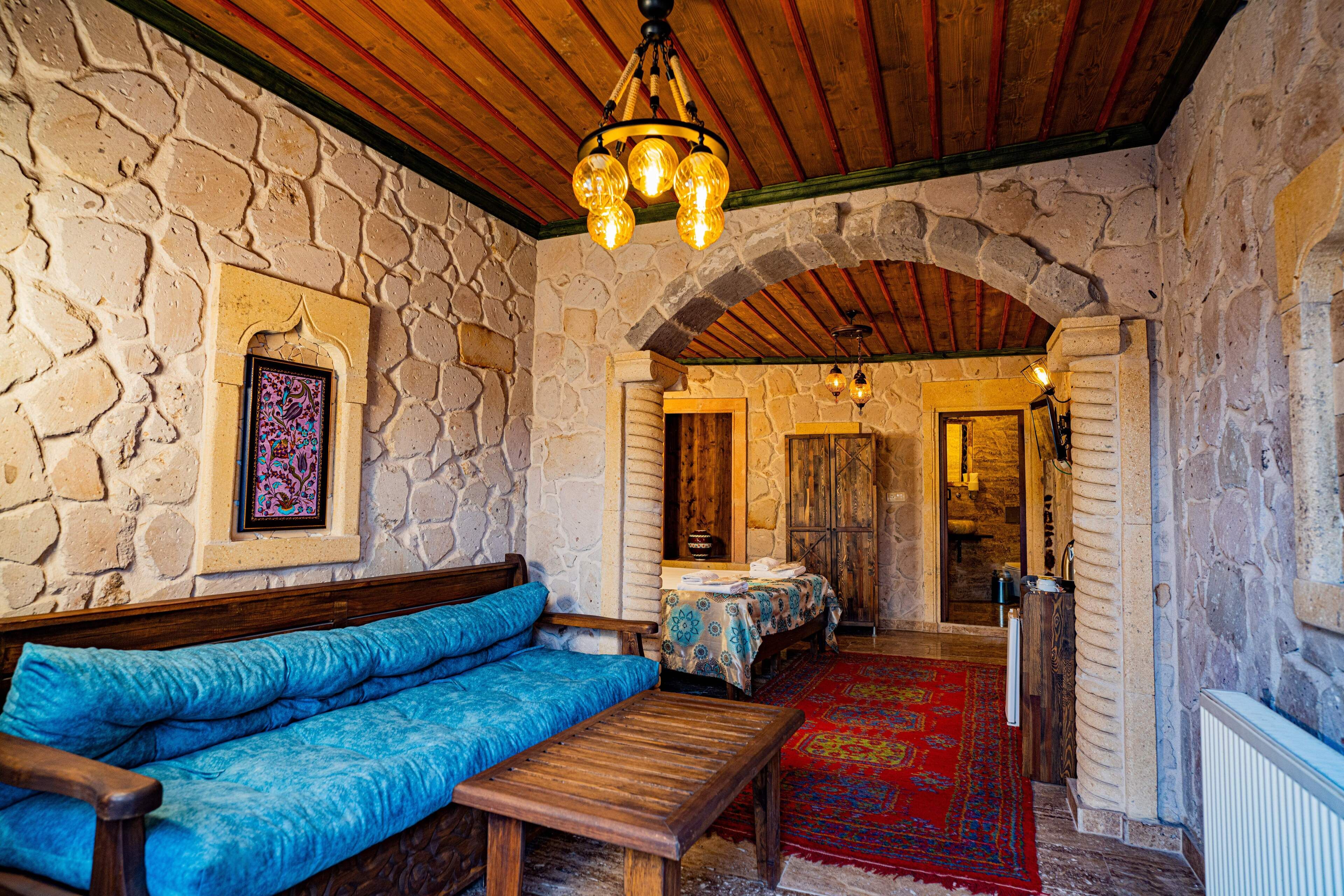 A stone-walled room with a wooden bench, a blue sofa, and a red carpet.