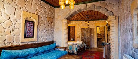 A stone-walled room with a wooden bench, a blue sofa, and a red carpet.