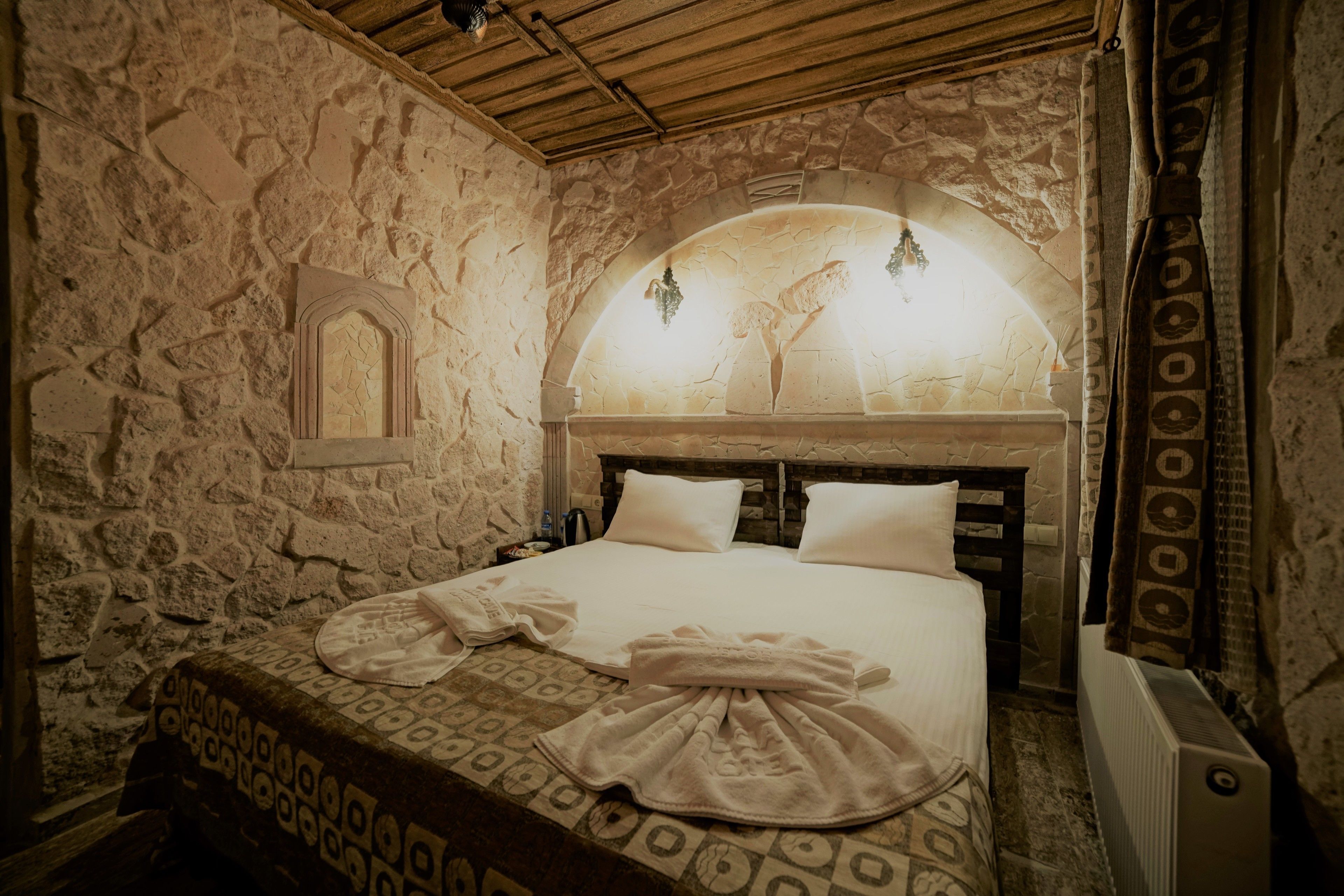 A stone-walled bedroom with a bed, a small window, and a decorative archway.