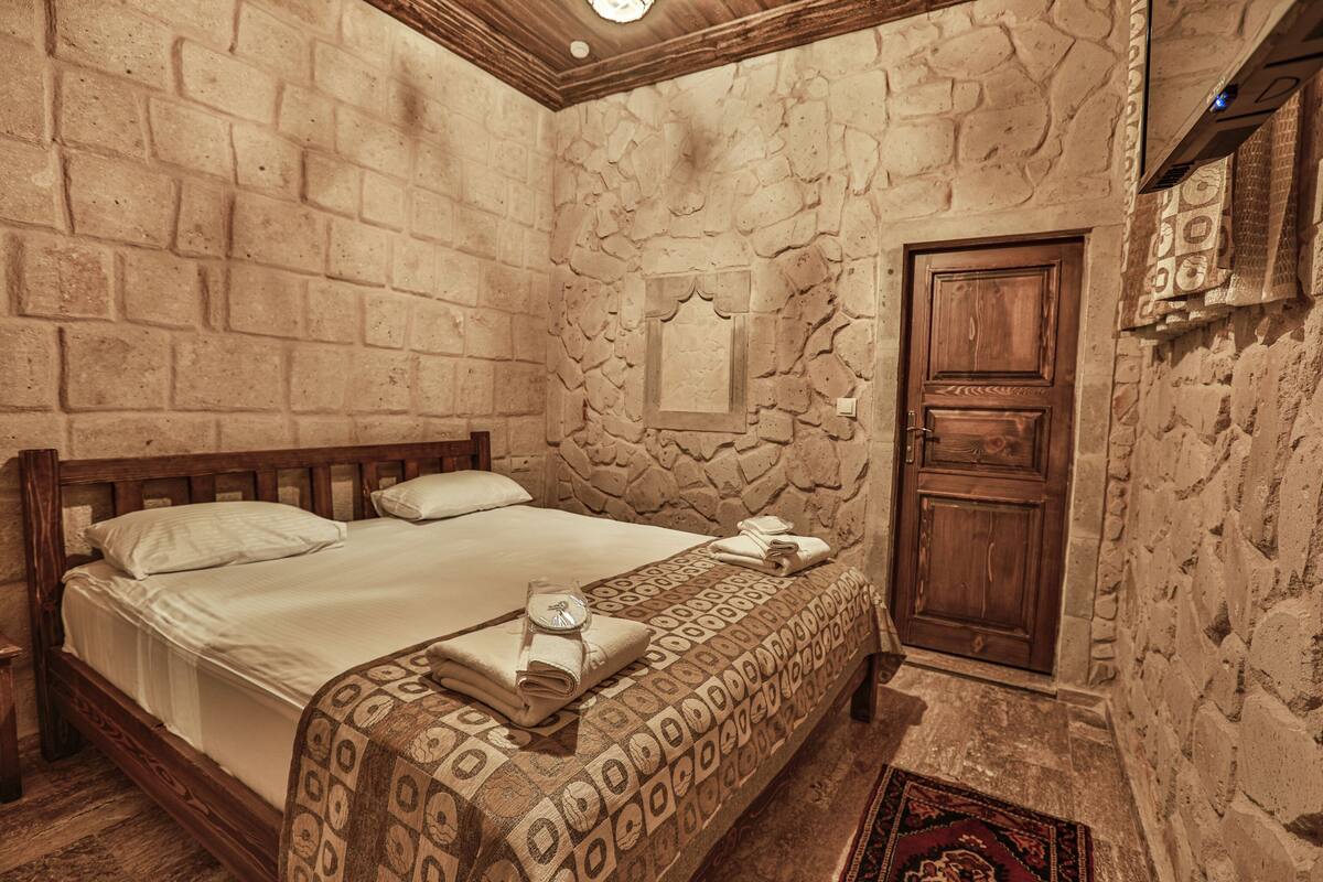 A room with a stone wall, a wooden bed with a patterned bedspread, and a wooden door.