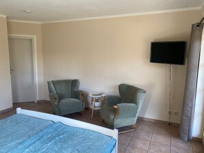 A room with a bed, two armchairs, a small table, a television, and a door. - Double room (apartment 2) - log cabin (Sangerhausen)