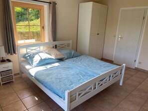 Quarto com cama, guarda-roupa, mesa de cabeceira e janela com cortinas.