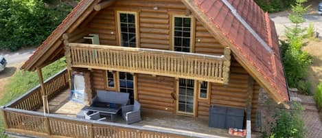 Una cabaña de troncos de dos pisos con balcón, mobiliario exterior y chimenea.