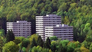 Zwei mehrstöckige Wohngebäude, umgeben von dichtem Wald.