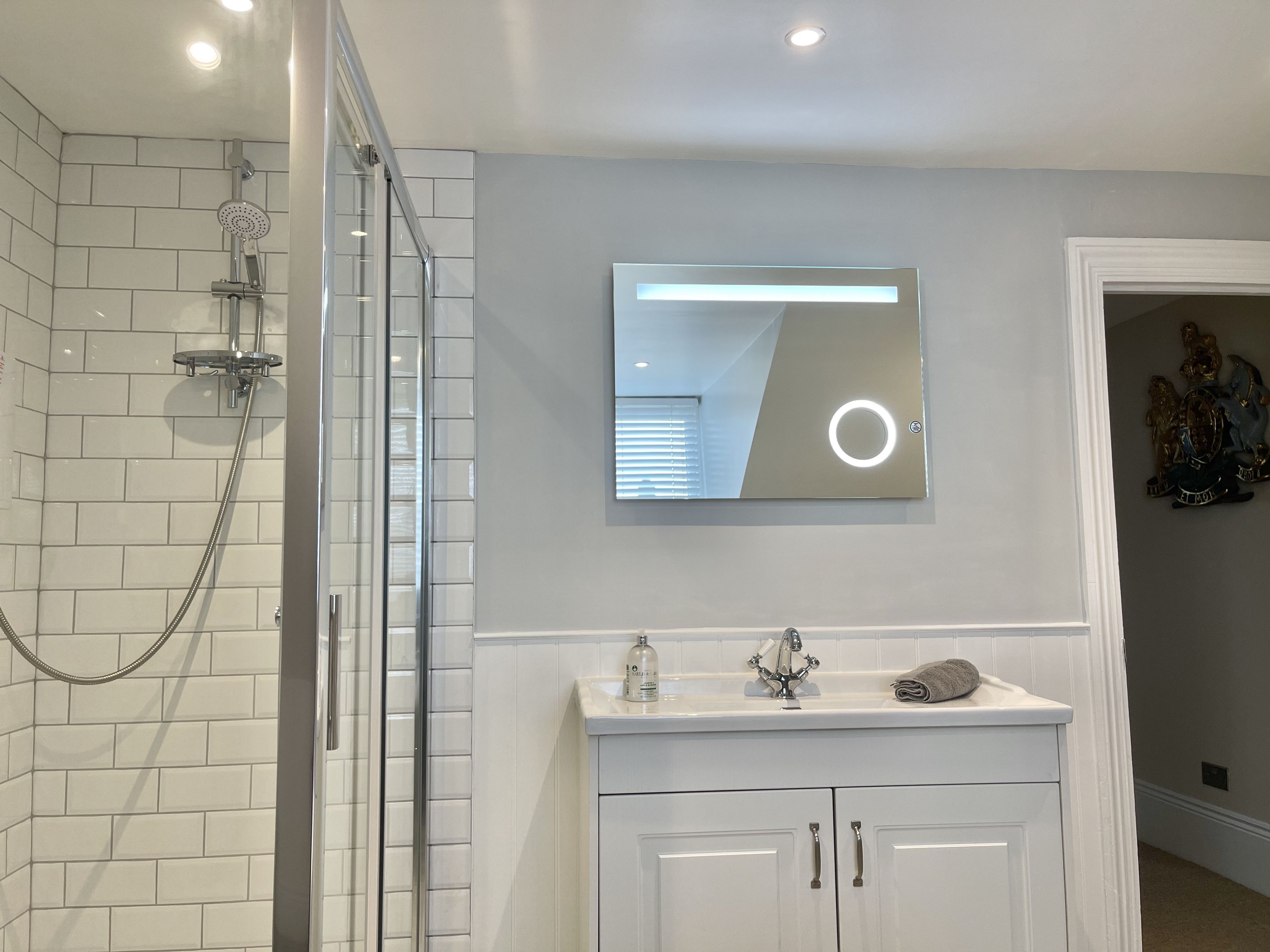 Une salle de bain moderne dotée d’une douche à parois de verre, d’un miroir fixé au mur et d’un meuble-lavabo avec des placards.