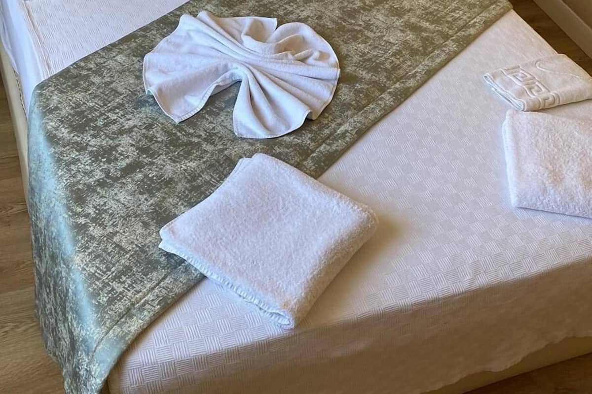 A neatly made bed with a decorative towel arrangement, a wooden headboard, and a bedside table with a phone.