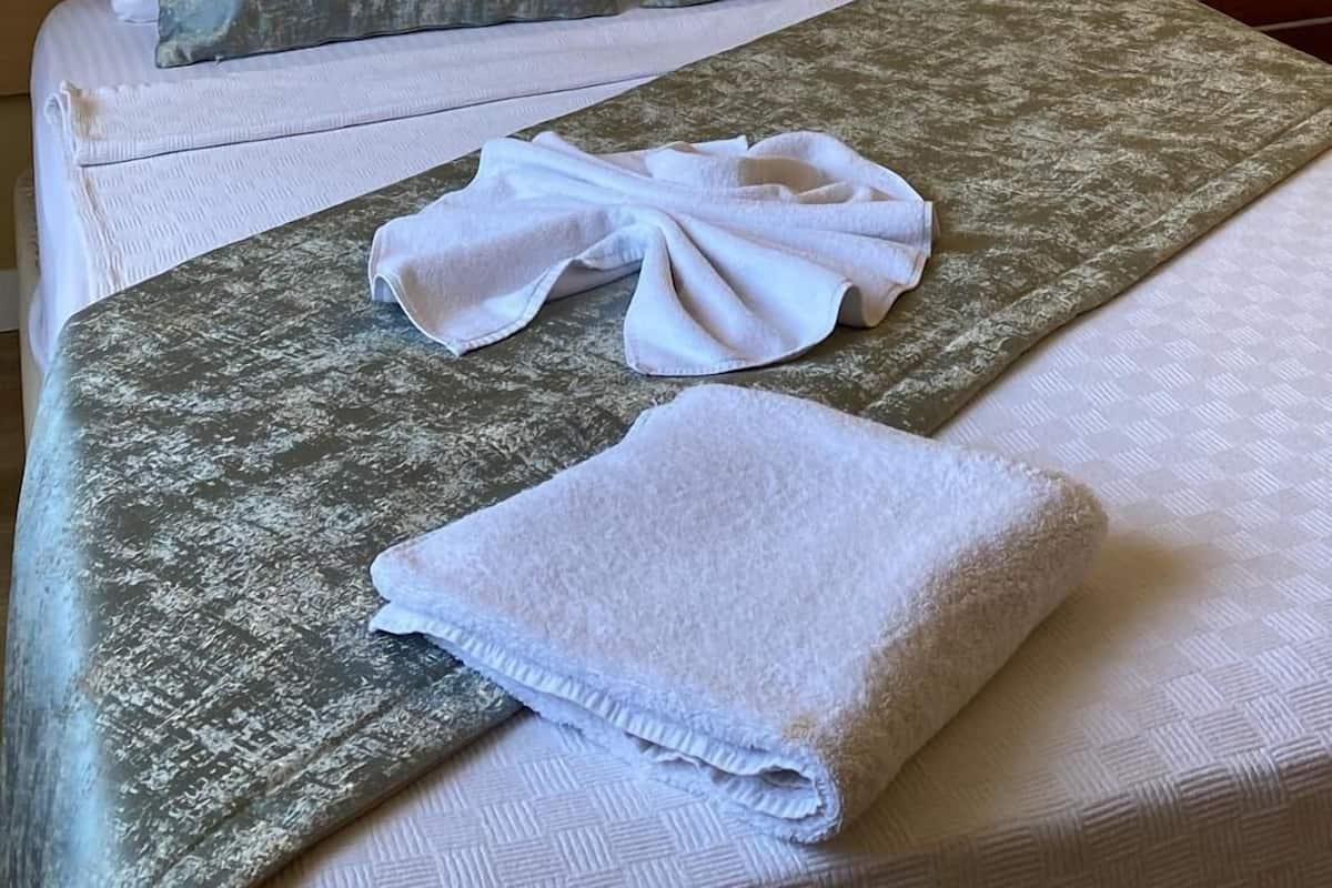 A hotel room with a bed, a painting of swans, a white headboard, and a bedside table with a phone.