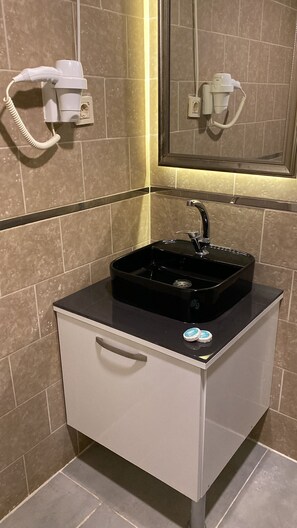 A bathroom with a black sink, a mirror, and a hairdryer mounted on the wall.
