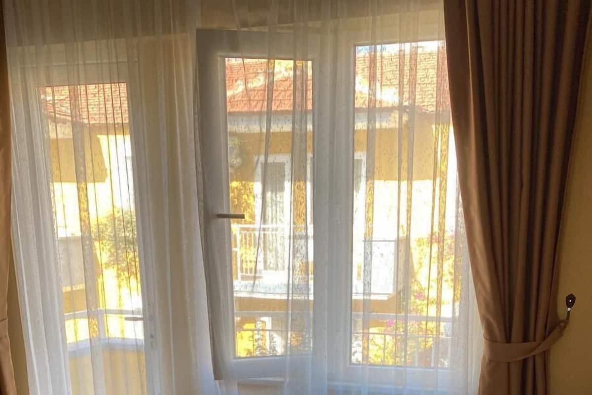 A bedroom with a bed, a sofa, a table, and a window with curtains.