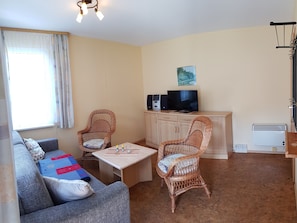 Un salon comprenant un canapé, deux fauteuils en osier, une table basse, un téléviseur et un meuble.