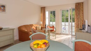 Una habitación con una mesa de comedor, un frutero, un sofá, un televisor y una ventana con cortinas.