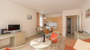 Un espacio habitable compacto con comedor, kitchenette y televisor sobre un escritorio.