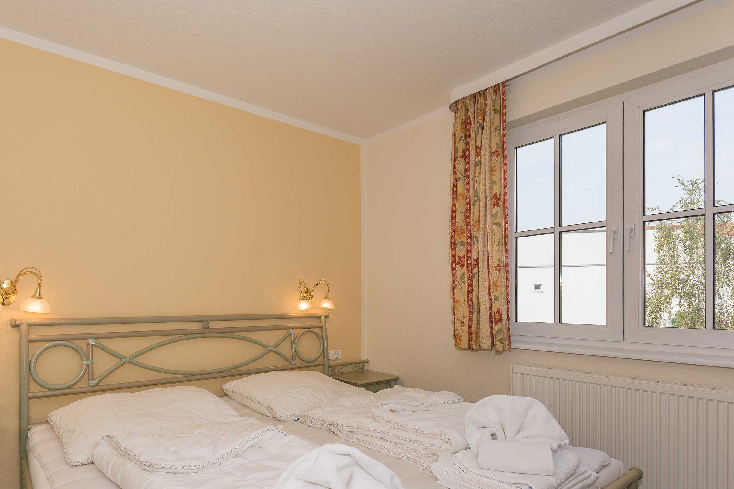 A bedroom with a bed, two bedside tables, a window with curtains, and a radiator.