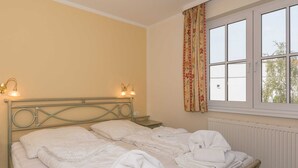 Un dormitorio con cama, dos mesitas de noche, una ventana con cortinas y un radiador.