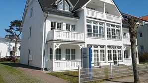 Un edificio blanco de dos pisos con un balcón, un letrero que dice "Jus Elise" y una entrada con portón.