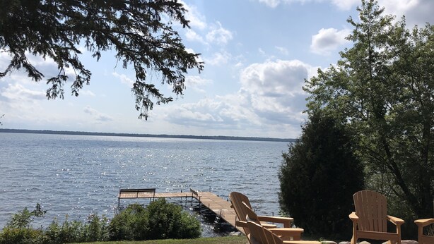 A lakeside view with wooden chairs and a dock extending into the water. - Private on Chain O’Lakes! Huge Kitchen, 2 Living Spaces, Large Cousins Room! (Lac Du Flambeau)