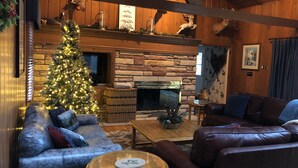 A cozy living room with a fireplace, leather sofas, a Christmas tree, and wooden walls. - Private on Chain O’Lakes! Huge Kitchen, 2 Living Spaces, Large Cousins Room! (Lac Du Flambeau)