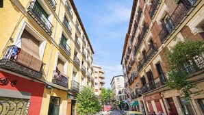 Una calle estrecha con edificios de varios pisos, balcones y coches aparcados.